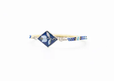 A handmade bracelet featuring a diamond-shaped blue centerpiece with floral inlay, complemented by a colorful woven band.