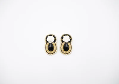 Elegant black and gold earrings featuring a white rose embellishment and teardrop-shaped gem centerpiece.
